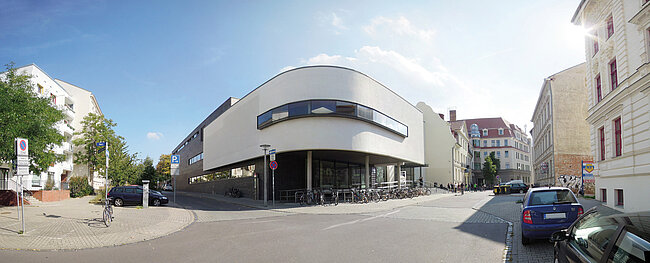 Harzmensa; Foto: Thomas Faust Ein modernes Gebäude mit weißer Fassade steht an einer Straßenecke. Vor dem Gebäude sind Fahrräder abgestellt und ein Auto fährt vorbei. Die umliegenden Gebäude sind aus Backstein und moderner Architektur. Die Szene wirkt ruhig und urban.